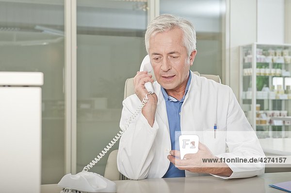Arzt telefoniert am Schreibtisch