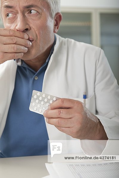 Arzt am Schreibtisch nimmt heimich eine Tablette ein