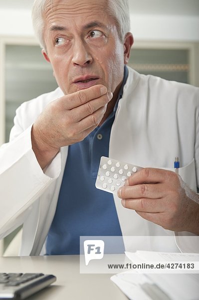 Arzt am Schreibtisch nimmt heimich eine Tablette ein