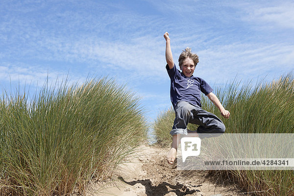Kleiner Junge beim Springen in Sanddünen