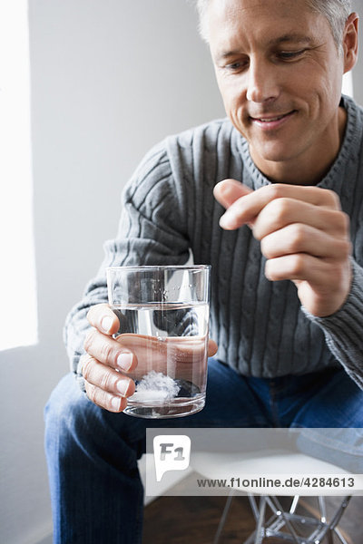Mann  der die Pille in ein Glas Wasser fallen lässt.