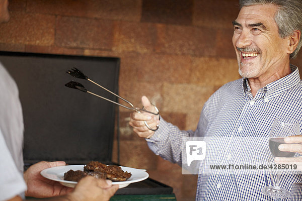 Happy older man serving up meat from BBQ