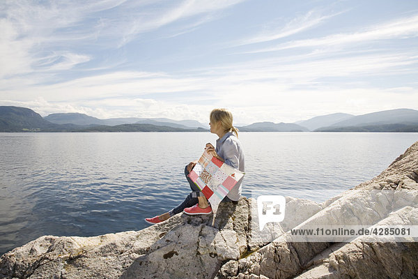 Woman sitting on rock by sea with kite