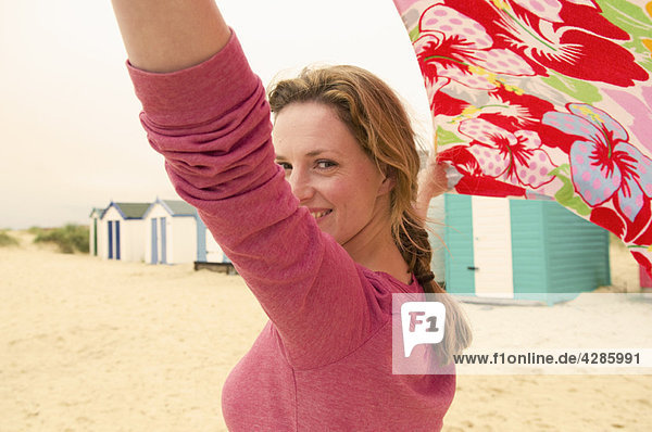 Glückliche Frauen am Strand halten Handtuch im Wind