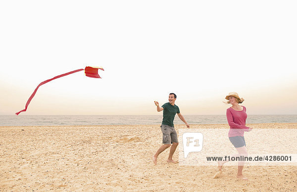 Happy couple fly kite on beach