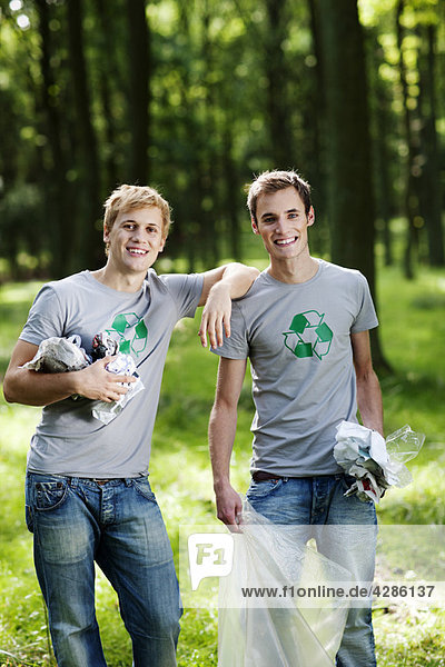 Two young men collecting trash in woods