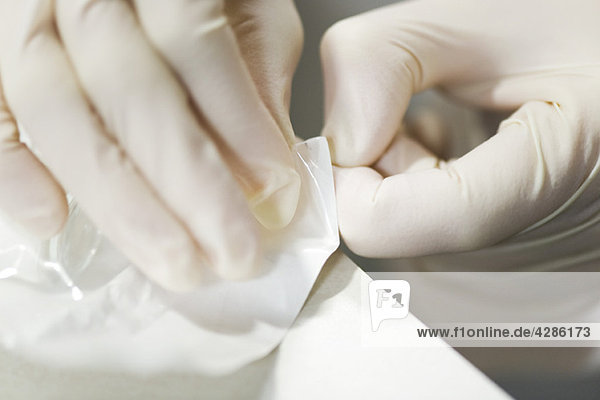 Gesundheitspersonal mit Latexhandschuhen  Öffnung der sterilen Verpackung mit medizinischem Zubehör