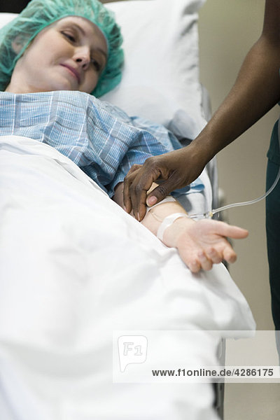 Patient watching as nurse checks IV needle placement in arm