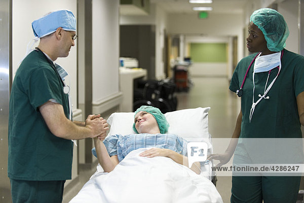 Arzt beruhigt Patientin auf Krankenhausbahre liegend