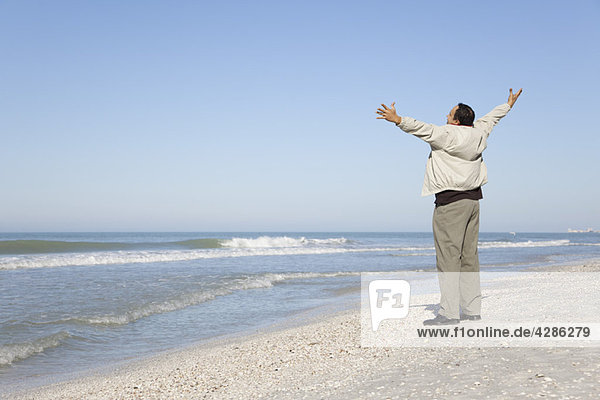 Man standing on beach looking at ocean with arms out