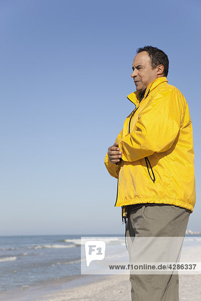 Erwachsener Mann steht am Strand und schaut auf das Meer.