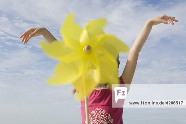 Girl standing outdoors with arms raised  face obscured by pinwheel in foreground