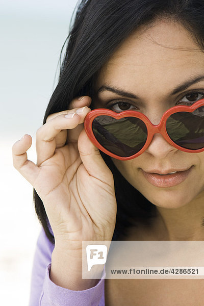Woman lowering heart shaped sunglasses to look at camera  portrait