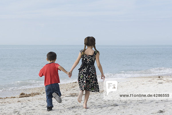 Kinder laufen zusammen am Strand und halten sich an den Händen.