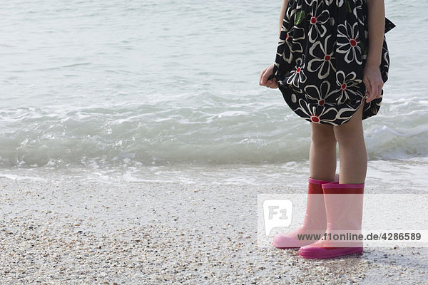 Mädchen am Strand stehend  mit Gummistiefeln