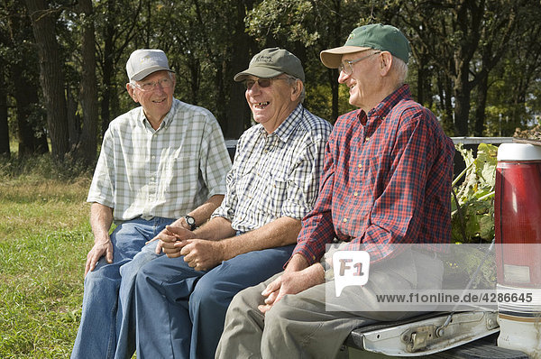 Three senior men sitting on the tail gate of a pick up truck in Manitoba