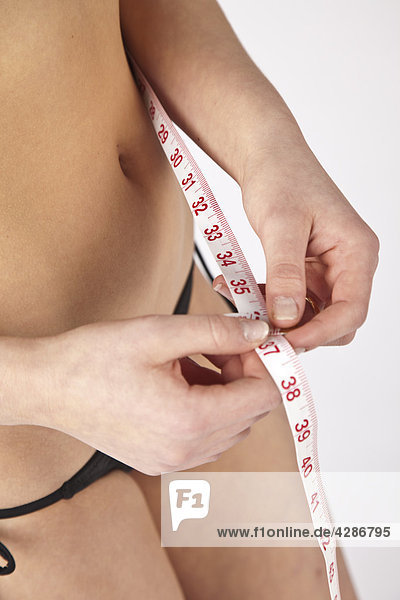 Woman's waist with hand and tape measuring her waist size
