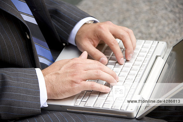 Business man in suit typing on laptop  outdoor setting