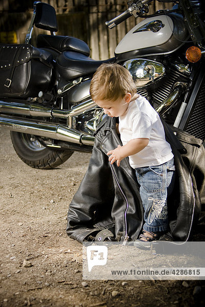 Small child holding Leather Jacket beside Motorcycle  outdoor setting