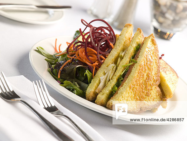 Sandwich und Salat mit Gedeck auf weiß Tischplatte