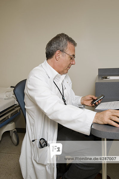 Doctor sitting at desk using mobile device in hospital examination room  Toronto  Ontario