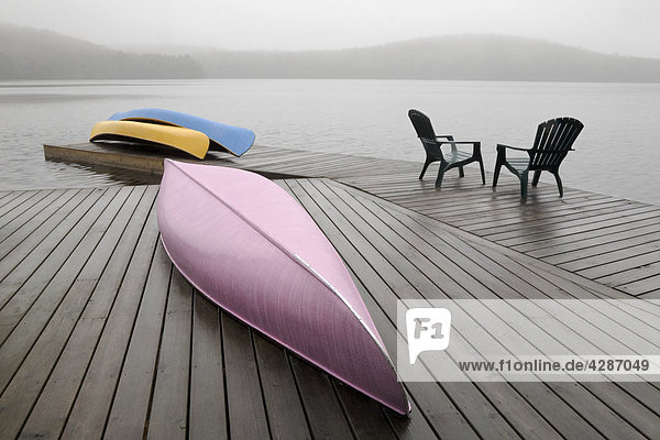Colourful canoes and chairs on dock on a misty morning  Algonquin Park  Ontario