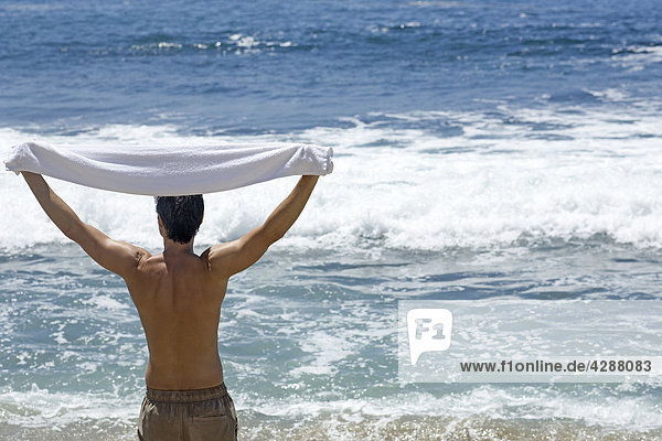 Mann mit Handtuch mit Blick auf den Pazifischen Ozean