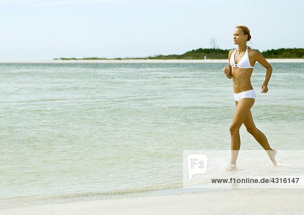 Woman in bikini running in surf at beach