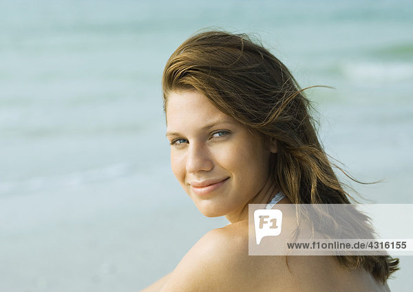 Junge Frau am Strand  über die Schulter lächelnd vor der Kamera