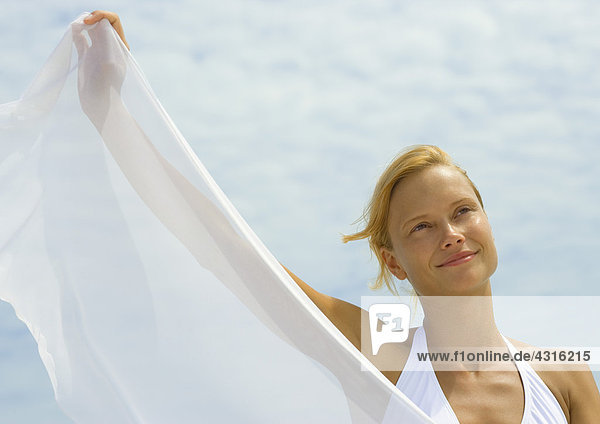 Frau hält durchsichtiges Tuch hoch  lächelnd  Himmel im Hintergrund