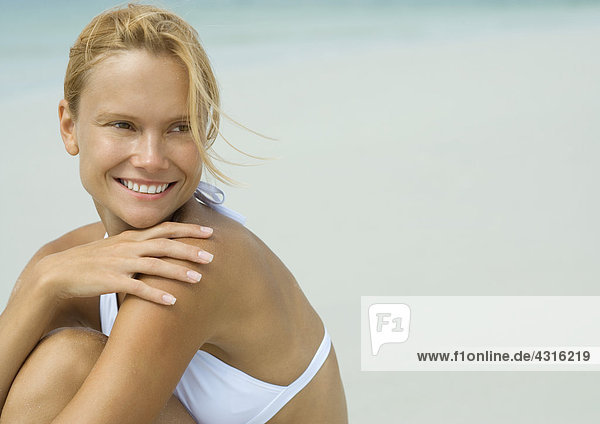 Frau im Bikini sitzend am Strand mit Hand auf Schulter
