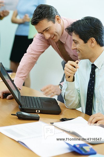 Business colleagues using laptop together  smiling