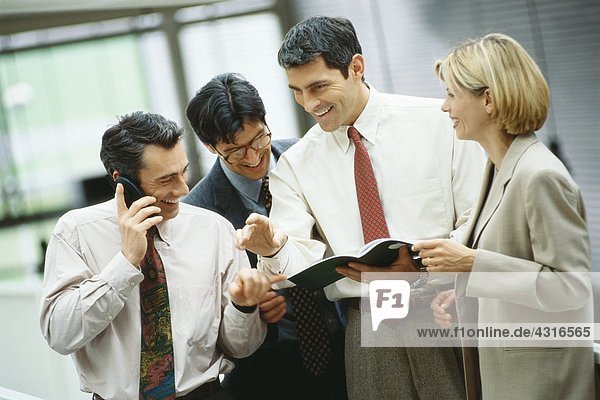 Four business colleagues standing looking at document while one uses phone