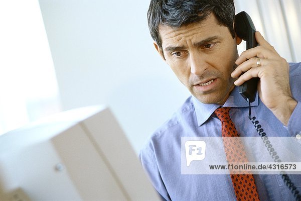 Businessman using phone  frowning and looking at computer