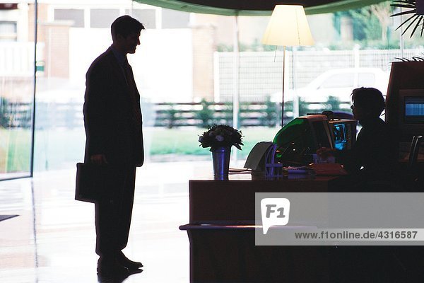 Businessman standing speaking to receptionist  silhouette