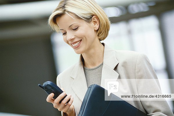 Businesswoman looking at phone  holding laptop