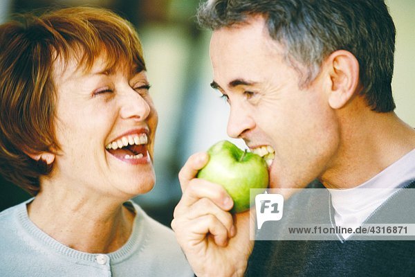 Senior man eating apple  senior woman laughing  close-up