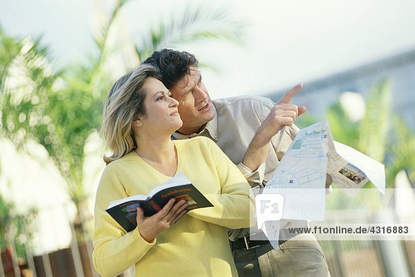 Erwachsenes Paar im Freien stehend mit Karte und Reiseführer  Mann zeigt auf