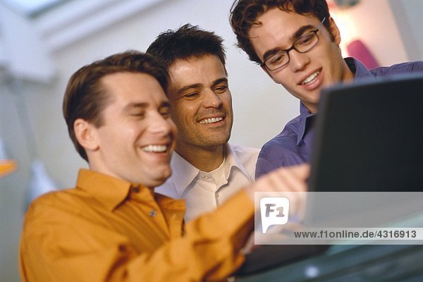 Three young men using laptop together