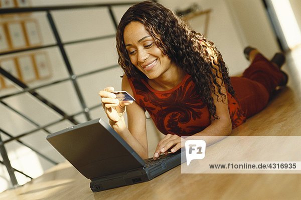 Junge Frau auf dem Boden liegend mit Laptop  Kreditkarte hochhaltend