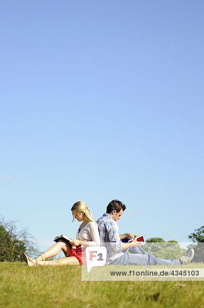 Paar sitzt Rücken an Rücken und liest im Park.
