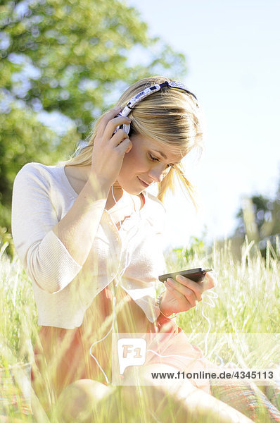 Junge Frau sitzt im hohen Gras und hört Kopfhörer.