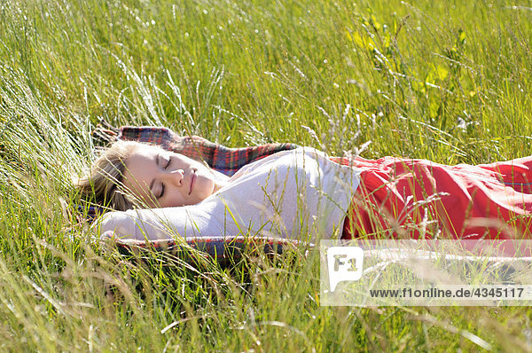 Junge Frau schlafend auf Decke im hohen Gras