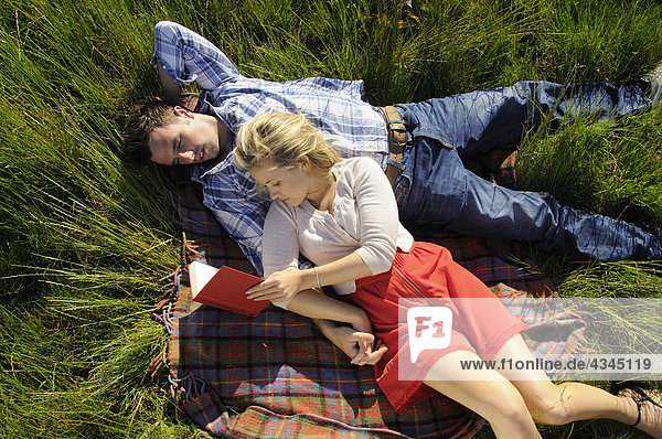 Couple lying on blanket reading together outdoors