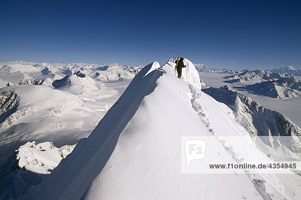 Male heli-skier stands atop snow covered ridge overlooking Chugach Mtn range SC Alaska Winter