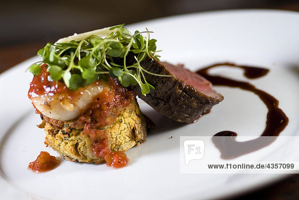 Kobe Beef Tenderloin Roasted and sliced and accompanied by bronzed Alaskan weathervane scallop and served over a Yukon Gold potato cake with fresh baby arugula  shaved Asiago cheese  balsamic veal reduction and roasted tomato preserves