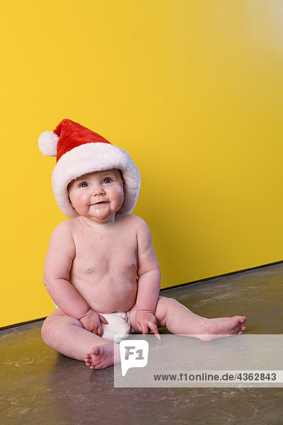Helligkeit Portrait Winter sitzend Boden Fußboden Fußböden Wand gelb Hut frontal Windel Säuglingsalter Säugling Kleidung Mädchen