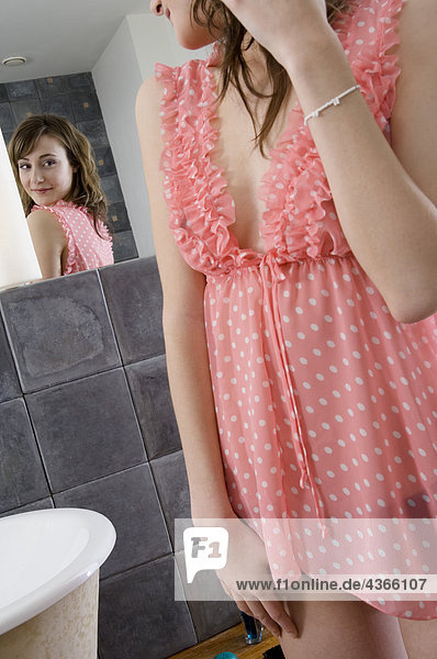 Junge Frau im Nachthemd vor dem Badezimmerspiegel