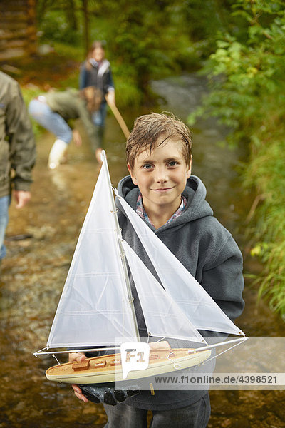Kleiner Junge mit Segelboot im Fluss