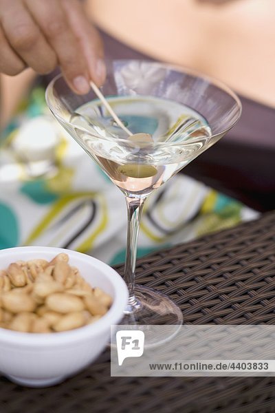 Frau hält grüne Olive auf cocktail-Stick in Martini-Glas